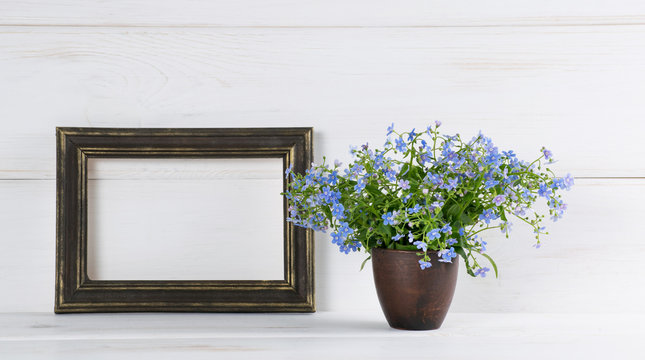 Me-nots flowers bouquet in clay vase and gilding photo frame on white wooden shabby board