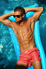 Man Summer Fashion. Beautiful Male With Sexy Body In Swimwear, Fashionable Sunglasses Tanning, Floating In Swimming Pool Water At Relax Spa Resort. Fitness Model With Skin Sun Tan Relaxing On Vacation © puhhha
