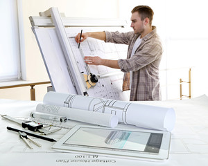 Table with construction drawings and male architect working on blueprints