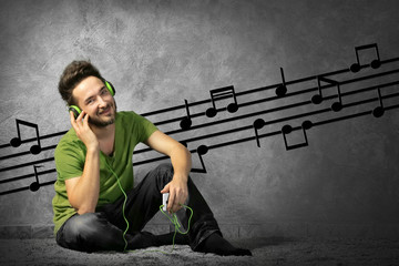 Young man with headphones listening to music sitting on grey wall background