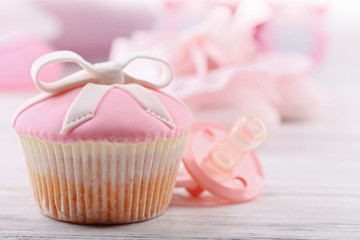Tasty cupcake with bow and baby shoes, decorative baby carriage on color background