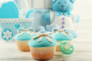 Tasty cupcakes with bow and baby shoes, decorative baby carriage and photo album  on color background