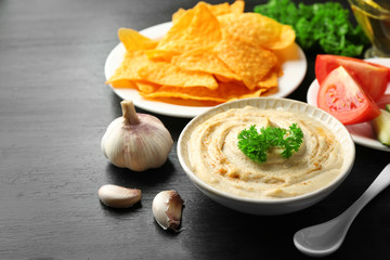 Ceramic bowl of tasty hummus with chips and parsley on table