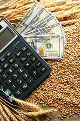 Dollar banknotes, calculator and wheat grains on wooden background. Agricultural income concept