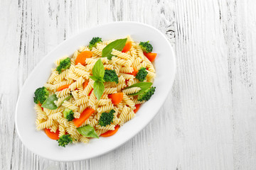 Boiled fusilli pasta with carrot, broccoli and basil on white plate