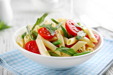 Boiled penne pasta with tomatoes, French bean and arugula on white plate