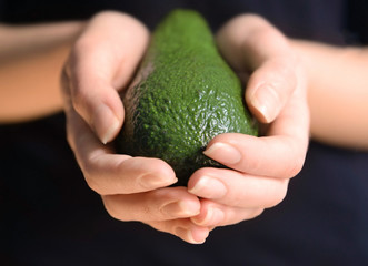 Female hands holding avocado on black background