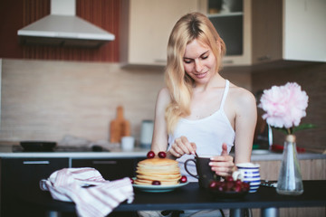 woman having breakfast in the kitchen tea with pancakes and cherries