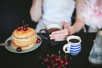 woman's hands holding a cup of tea. Breakfast of pancakes in the kitchen.