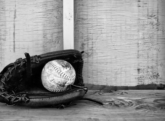 A softball laying in the pocket of a ball glove on a wood bench in black and white - obrazy, fototapety, plakaty