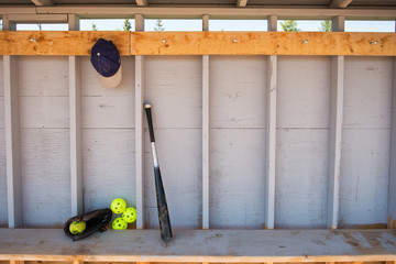 Baseball bat, hat, glove and ball leaning against a wall in a baseball dugout - obrazy, fototapety, plakaty