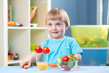 Cute little boy eats carrot and other vegetables in room