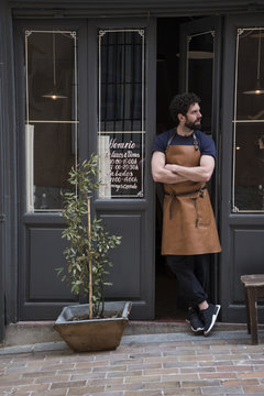 Craftsman with leather apron and arms crossed standing at the entrance of his workshop