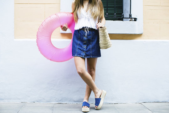 Young woman standing with bathing ring and beach bag