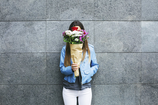 Young woman holding bunch of flowers in front of her face