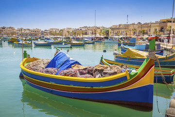 Malta - Traditional colorful Luzzu fishing boats at Marsaxlokk on a nice summer day with blue sky and crystal clear green sea