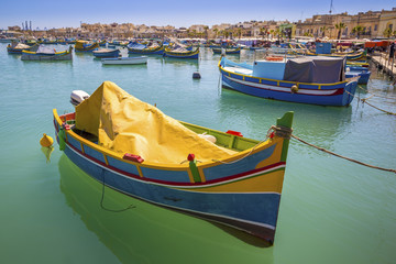Fototapeta na wymiar Malta - Traditional colorful Luzzu fishing boats at Marsaxlokk on a nice summer day with blue sky and crystal clear green sea