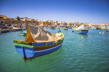 Fototapeta na wymiar Malta - Traditional colorful Luzzu fishing boats at Marsaxlokk on a nice summer day with blue sky and crystal clear sea