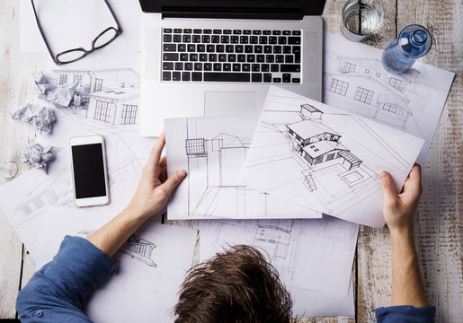 Architect working at desk with laptop, looking at sketches