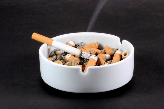 White ceramic ashtray full of smokes cigarettes. Selective focus.