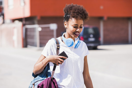 Smiling young woman wearing headphones and holding cell phone outdoors