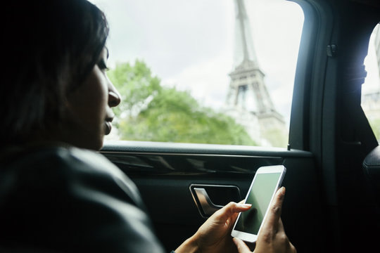 France, Paris, young woman sitting in a car looking at her smartphone