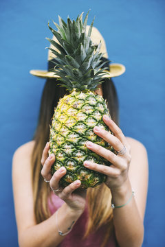 Young woman holding pineapple  in front of her face