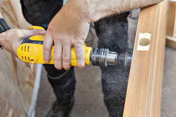 Hands working with electric drill, boring large hole of doorlock