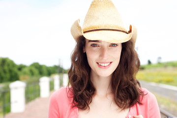 Smiling young woman standing in cowboy hat outside