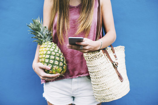 Young woman holding cell phone and pineapple