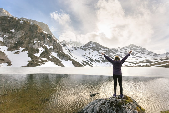 Spain, Asturias, Somiedo, woman standing with raised arms at mountain lake