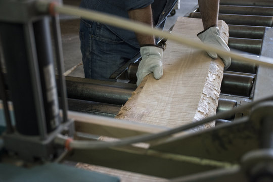 Man with gloves putting a wood plank on an industrial circular saw in a factory
