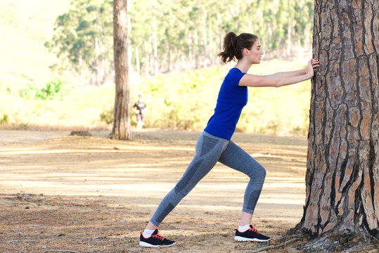 Sporty woman pushing against tree