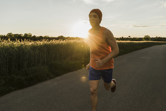 Germany, young man jogging, against the sun