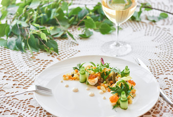 Russian salad served on a white plate and a glass of white wine on table close-up