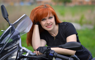 Fototapeta na wymiar Interesting,cheerful,smiling,pretty,nice,good,friendly,lovely,adorable,redhead,red-haired professional biker girl with black,fast motorcycle,motorbike,bike,cute smile.Girl with motorbike,fast rider.