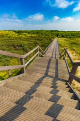 Fototapeta na wymiar Wooden staircase going into blue sky among dunes and high grass, De Haan, Belgium