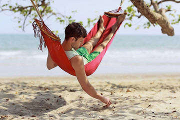Young man resting in hammock on beach