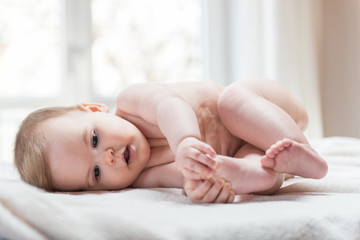 Cute baby child lying on white sheet and holding his legs