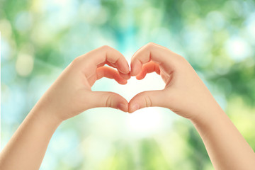 Child hands in shape of heart on green nature background.