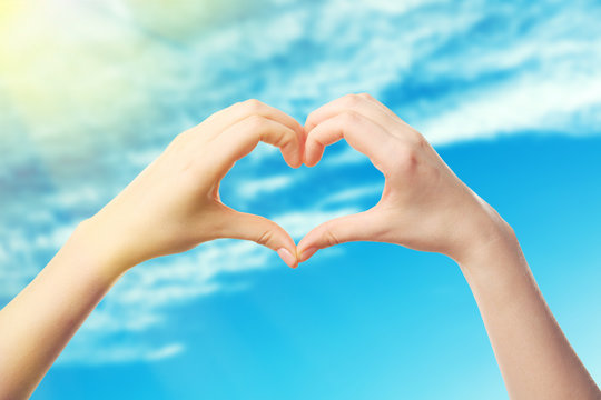 Female hands in shape of heart, on blue sky background
