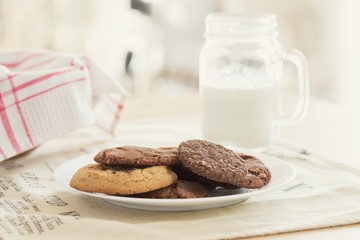 Mix of homemade chocolate chips and cookies with milk over the dining table to take a snack in afternoon.