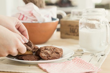 Hands breaking a homemade chocolate cookie over the dining table to take a snack