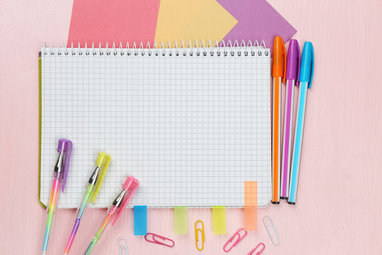 Office set with notebook, colored pens and clips on pink background