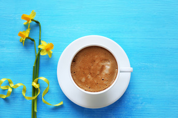 Cup of coffee and daffodils on blue wooden background