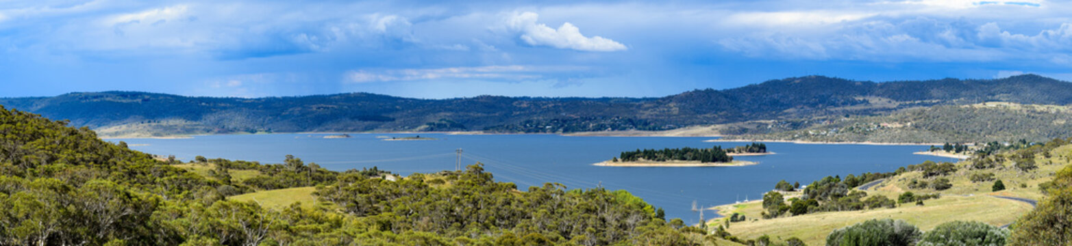 Lake Jindabyne landscape with a blue overcast sky and green rural foreground.  Featuring a number of islands including the two largest -  'Lion Island' and part of 'Cub Island'.