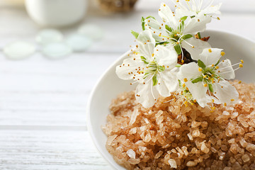 Brown sea salt with blooming flowers on wooden table