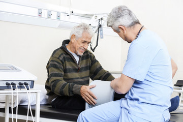 Physiotherapist Examining Senior Patient On Bed