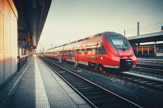Fototapeta Beautiful railway station with modern red commuter train at colorful sunset in Nuremberg, Germany. Railroad with vintage toning