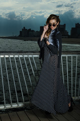 Attractive young woman wearing black and white maxi dress, posing on the pier, with effective clouds and lighting from coming thunderstorm.